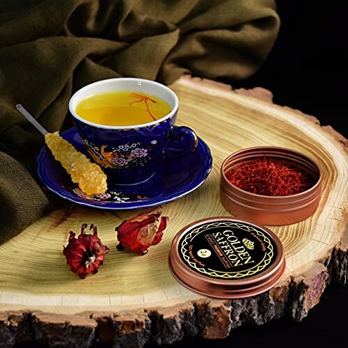 Cup of saffron tea with honey stick and saffron container on wooden slab.